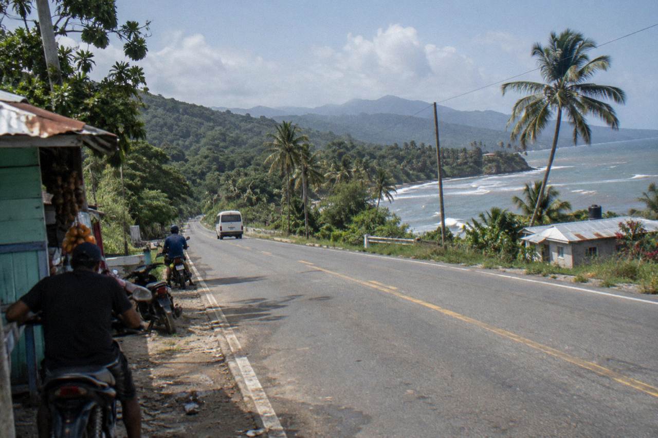 Two-lane highway in northern Dominican Republic with green hills, palm groves and motoconchos