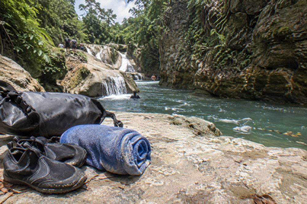 Water shoes, towel and dry bag arranged on a bench beside a canyon trail