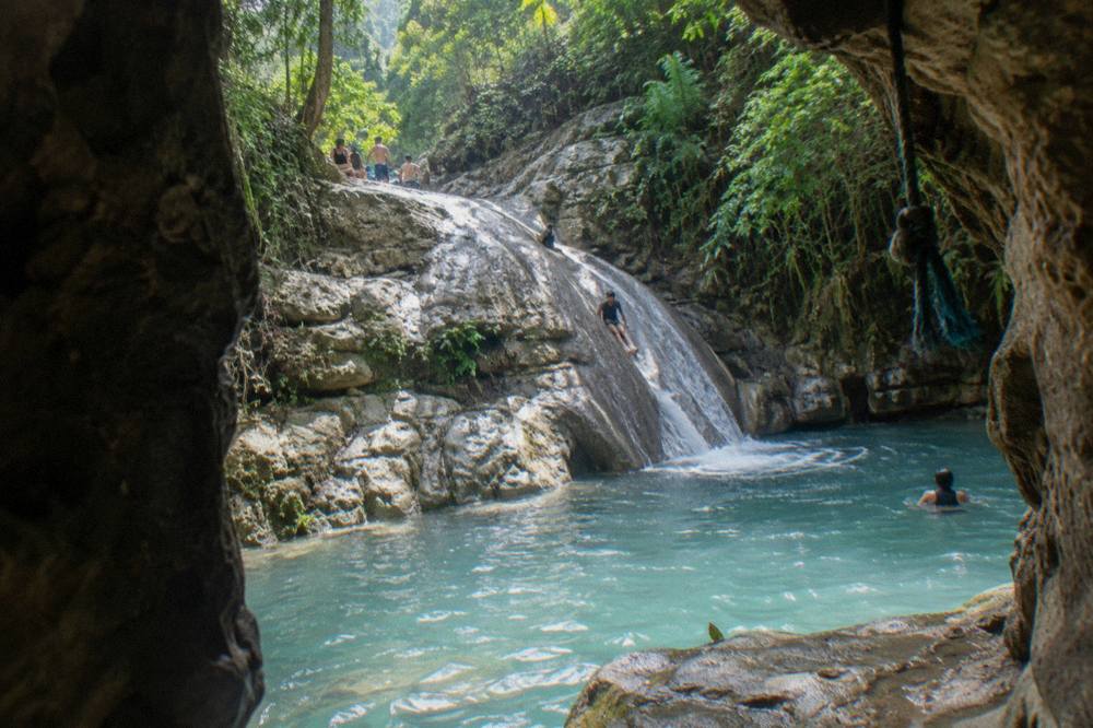 Turquoise pool at the base of a rocky canyon slide surrounded by dense green forest