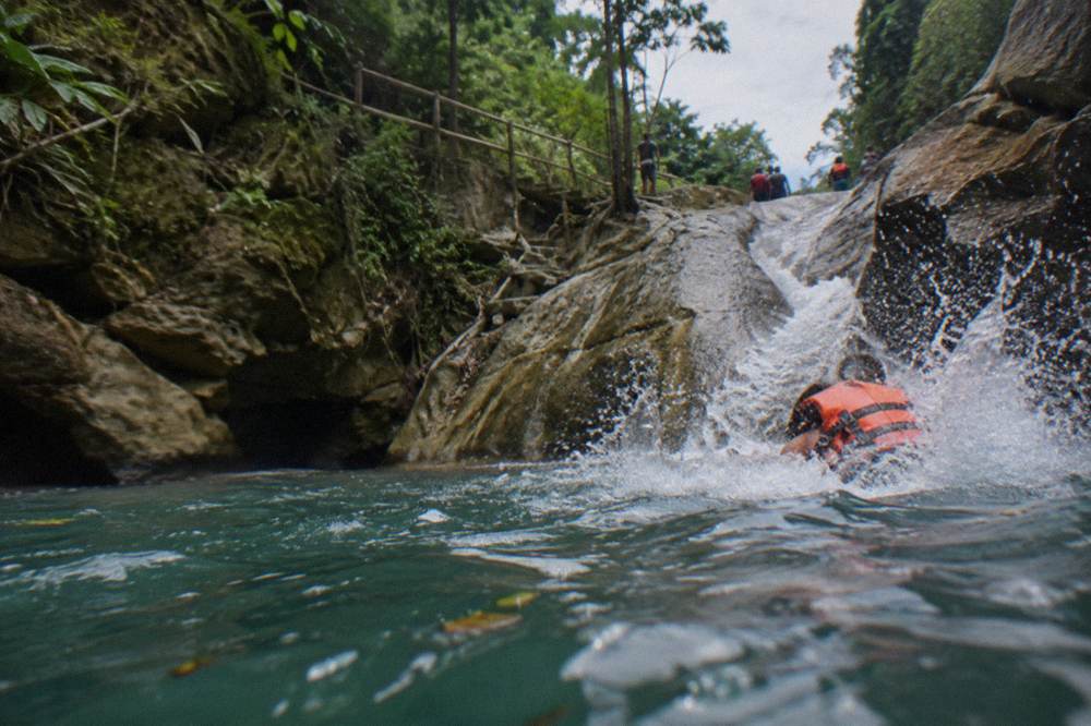 Small group in orange life jackets sliding down a smooth rock chute into a deep pool