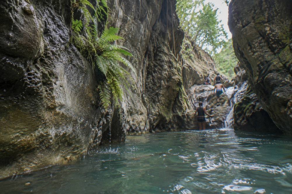 Narrow canyon walls rising above a clear turquoise pool at Damajagua