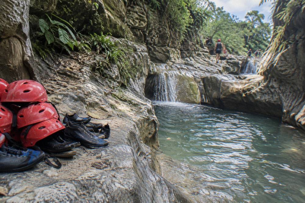 Water shoes and helmets stacked on wet rock beside a pool at Damajagua