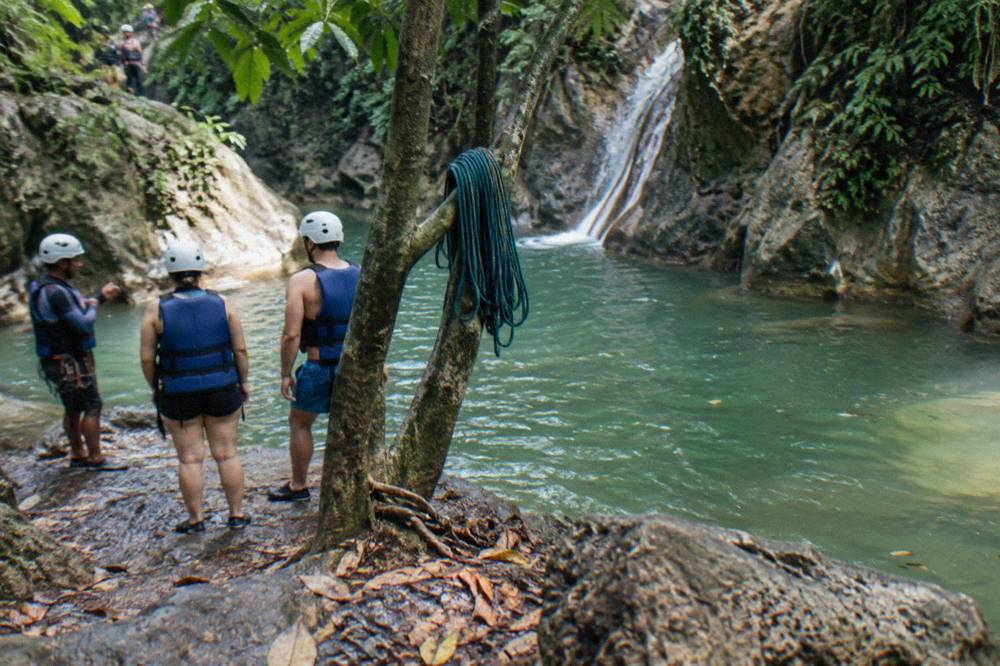 Guides in helmets and life jackets briefing visitors beside a jungle river pool