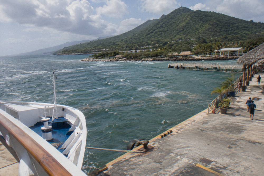 Cruise ship anchored at a Caribbean port terminal with hills behind