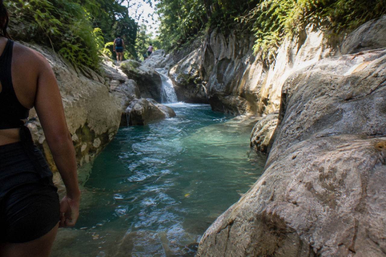 Turquoise waterfall pool in a narrow forested canyon with limestone walls