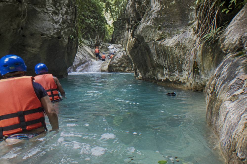 Cascading turquoise water spilling over limestone ledges into a deep pool inside a green canyon