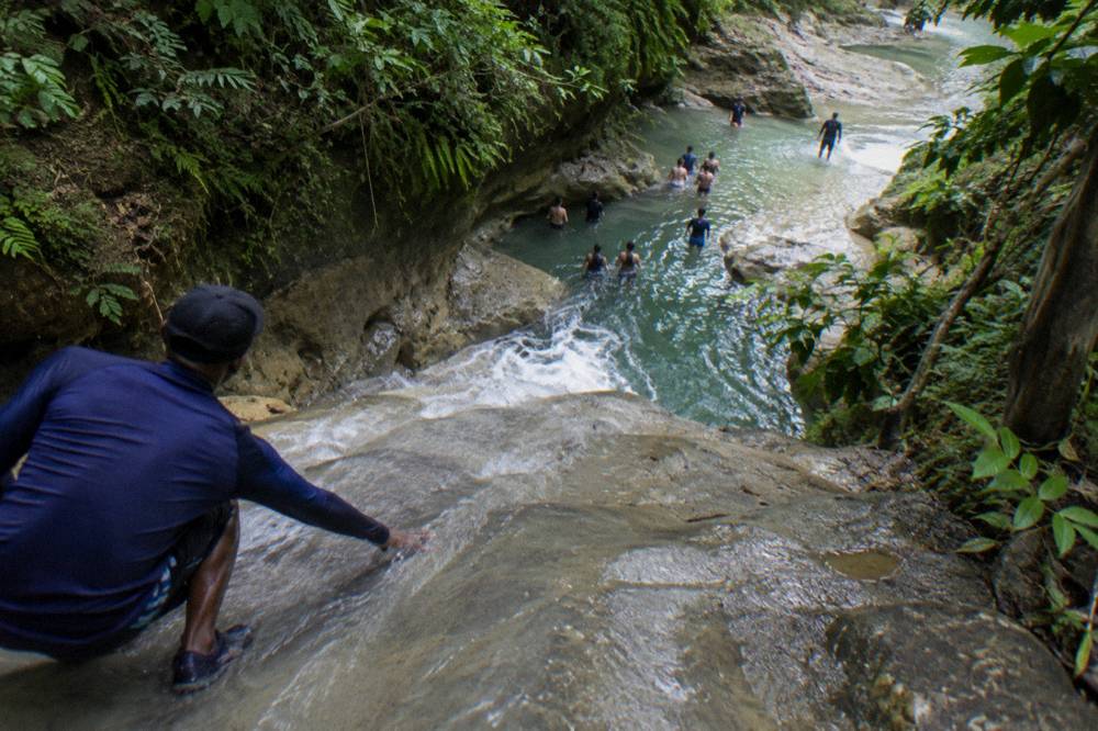 Sunlight falling on a series of stepped waterfalls and calm blue swimming holes in a forest gorge