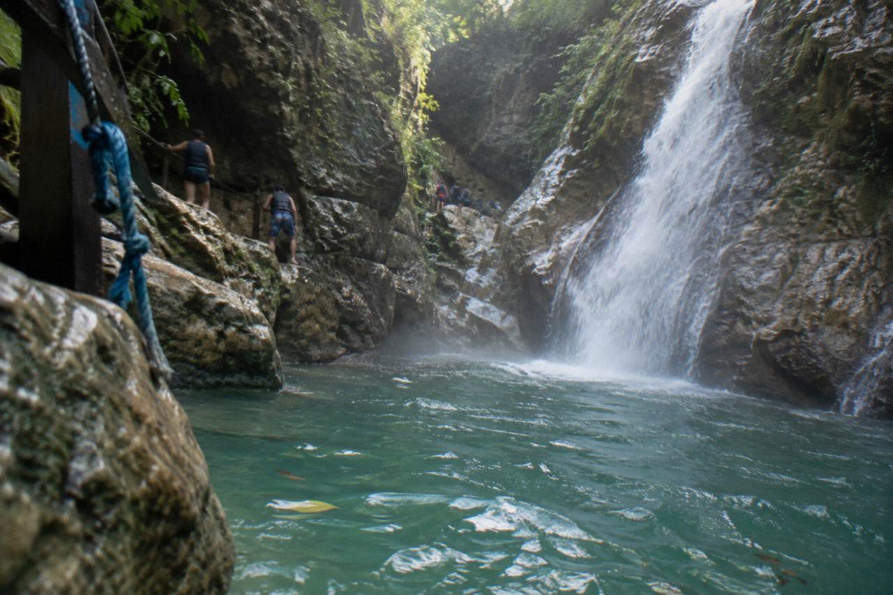 Turquoise waterfall pool winding through a narrow forested canyon in the Dominican Republic