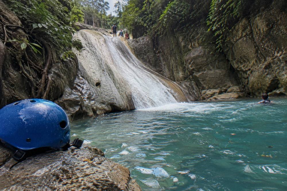 Clear blue pool at the base of a rock slide in a green canyon