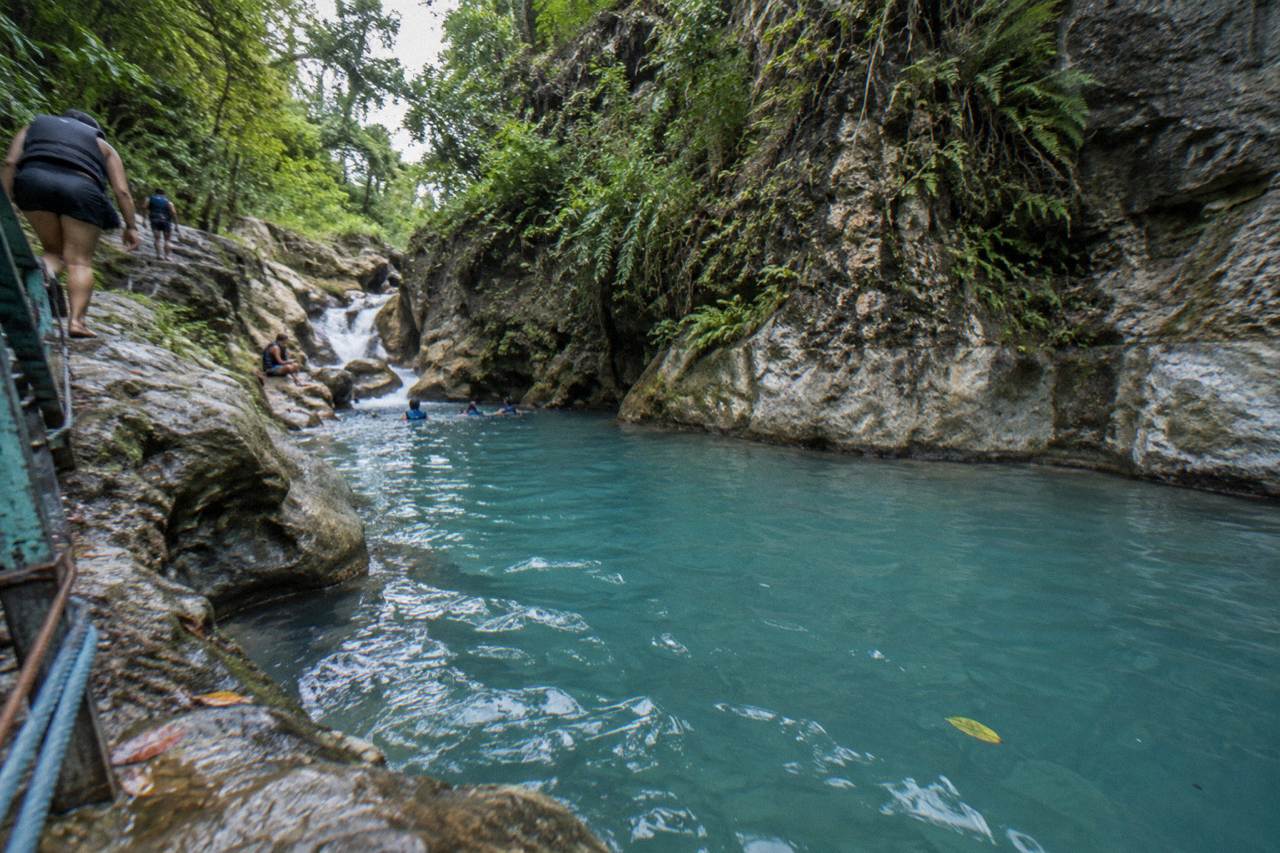 Turquoise waterfall pool in a narrow forested canyon with rocky walls