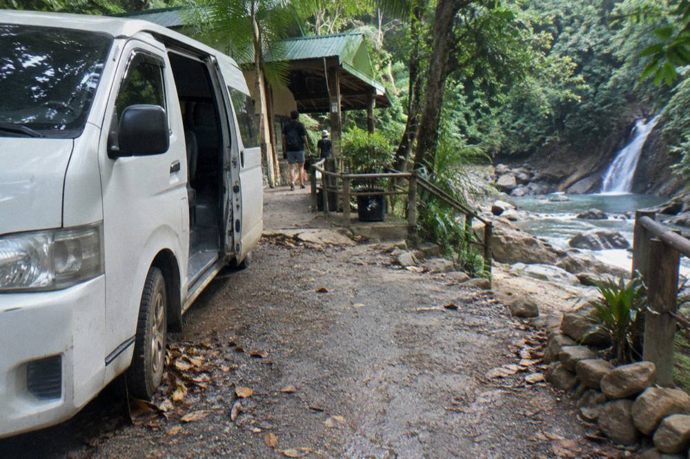Air-conditioned tour van parked on a forest road near the waterfall entrance