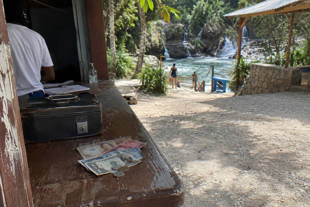 Dominican pesos and US dollar notes held in hand at an outdoor ticket counter