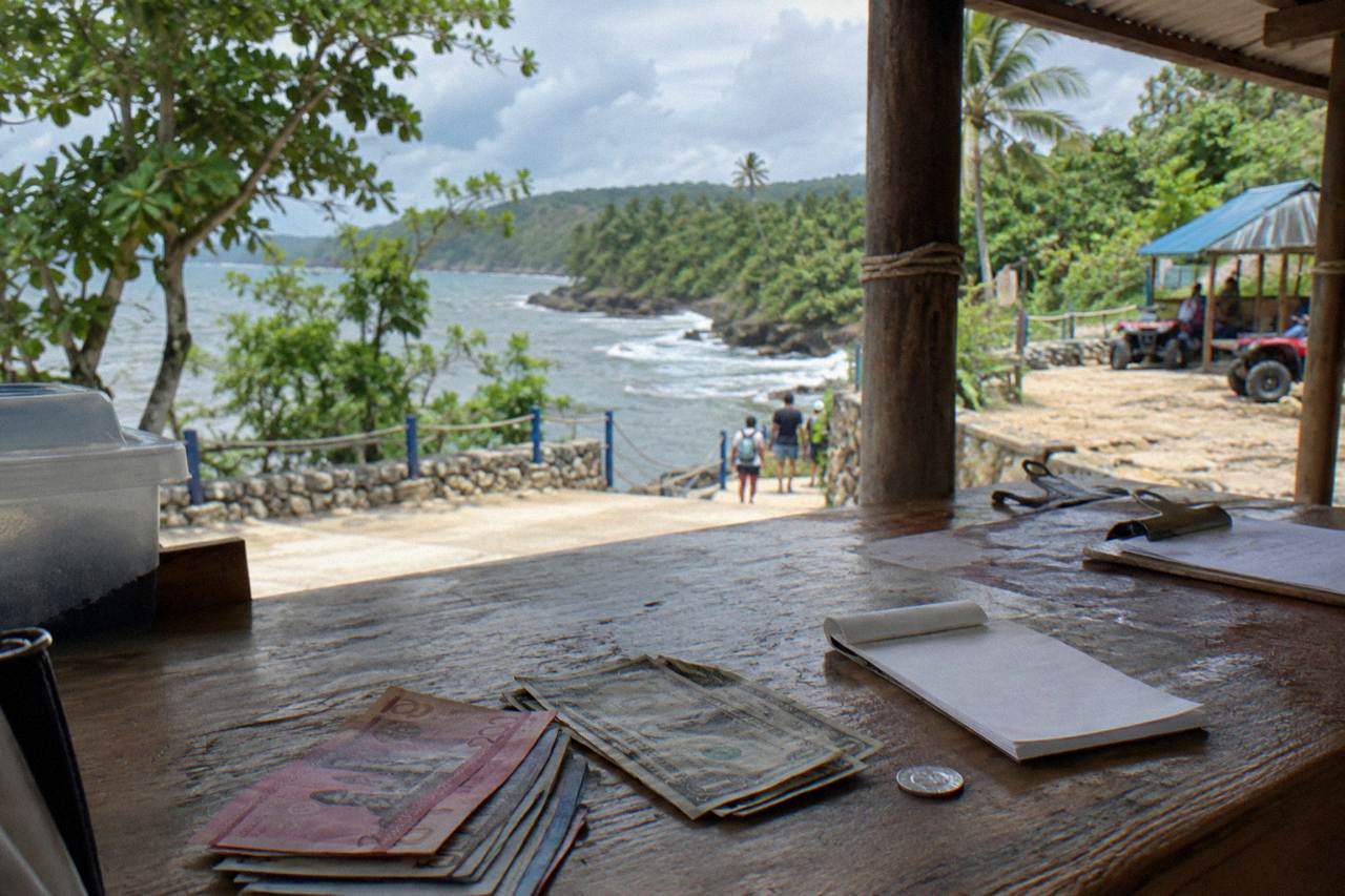 Worn wooden counter at the Damajagua visitor centre with peso and dollar notes, a receipt pad and a coin