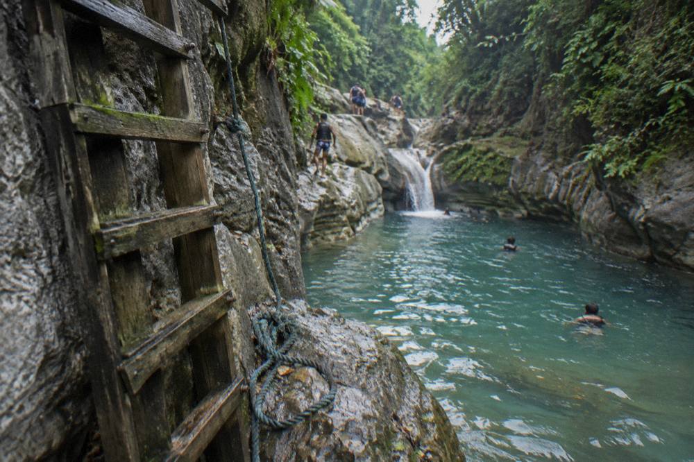 Wooden ladder beside a rock face leading down to a clear canyon pool
