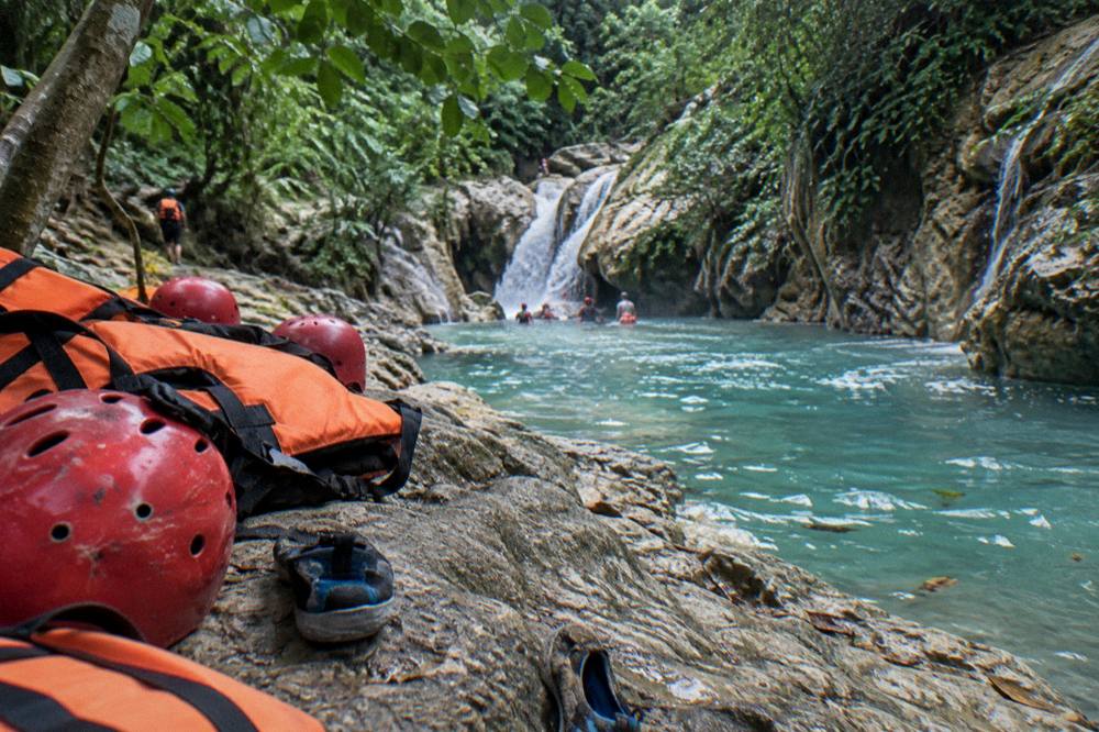 Helmets and life vests on rocks beside a calm turquoise pool