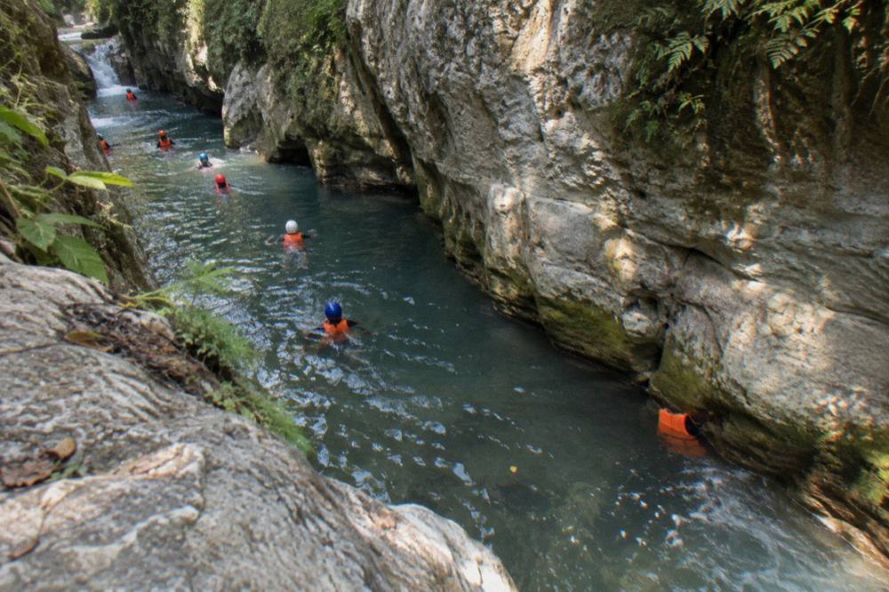 Swimmers in helmets and life jackets floating in a narrow canyon pool