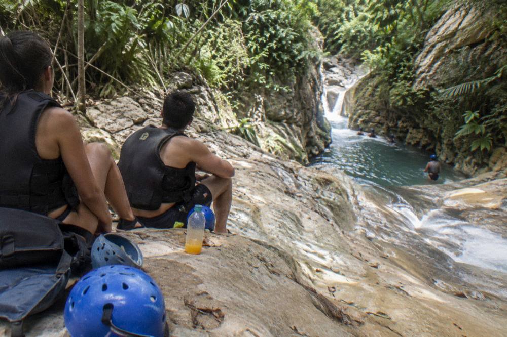 Small group resting on rocks beside a waterfall chute in helmets and vests