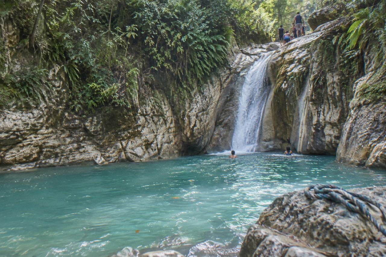 Turquoise pool at the base of a jungle waterfall surrounded by limestone rock