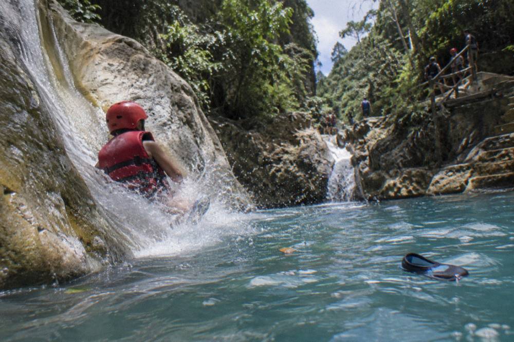 Child in a helmet and life jacket sliding into a clear blue pool