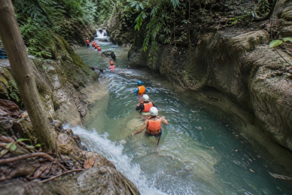 Guided group in helmets and life jackets walking through a green river canyon