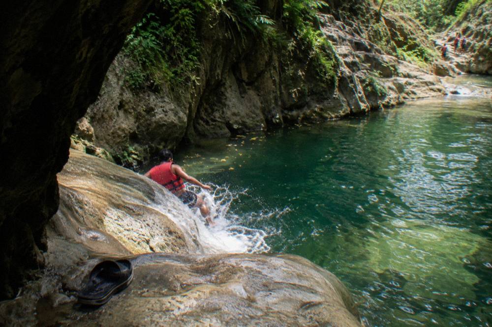 Swimmer in a life jacket sliding down a smooth rock chute into a deep pool