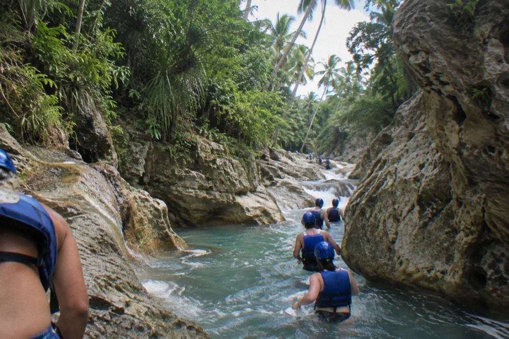 Guided group in helmets and life jackets walking through a jungle river between rock walls