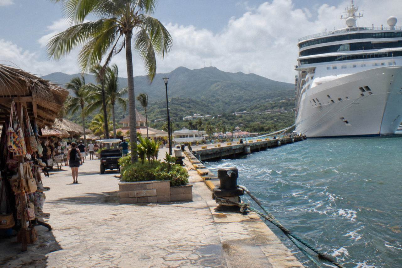 White cruise ship berthed at the Taino Bay pier in Puerto Plata with souvenir market stalls, palms and green foothills behind