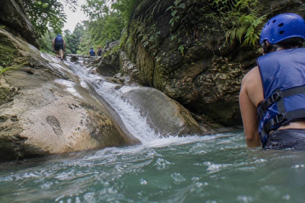 Canyon visitor in helmet and life jacket sliding down a rock chute into a green pool