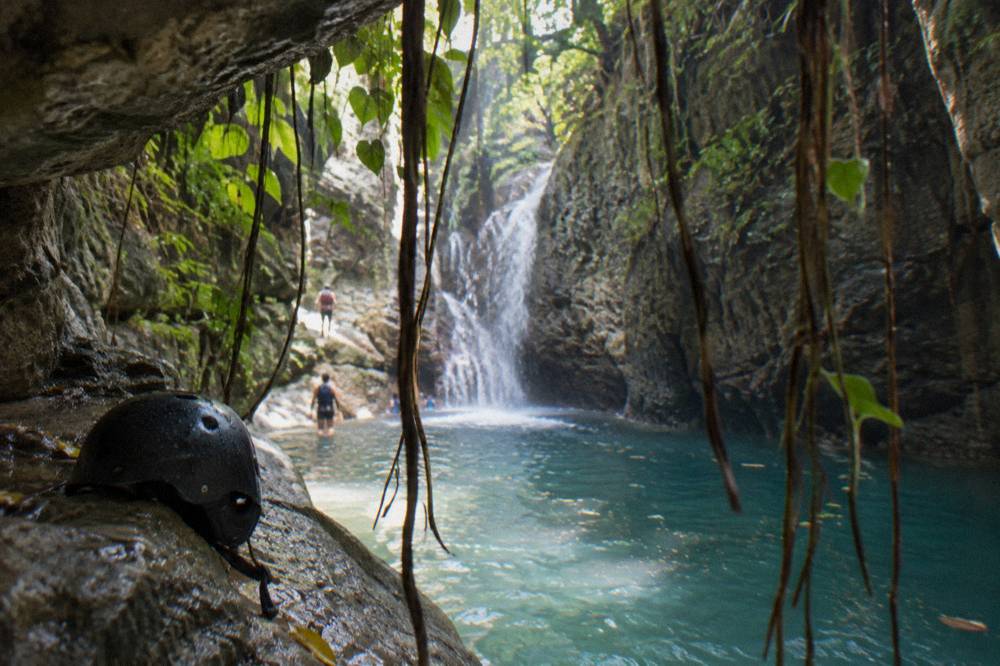 Turquoise pool at the base of a waterfall framed by tall canyon walls and hanging vines
