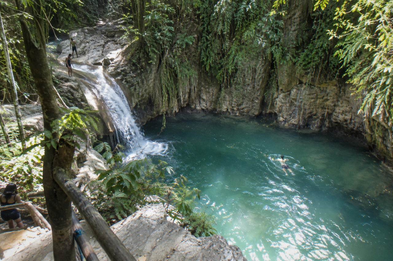 Turquoise waterfall pool in a narrow forested canyon with limestone walls