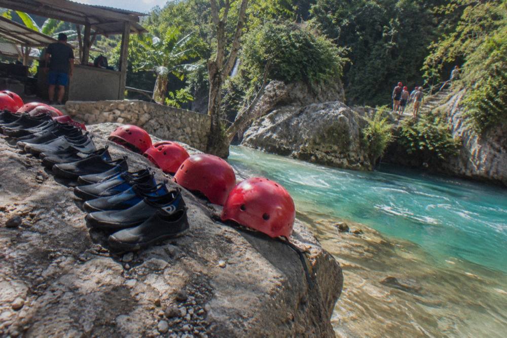 Water shoes and helmets lined up on a rock beside a clear turquoise pool