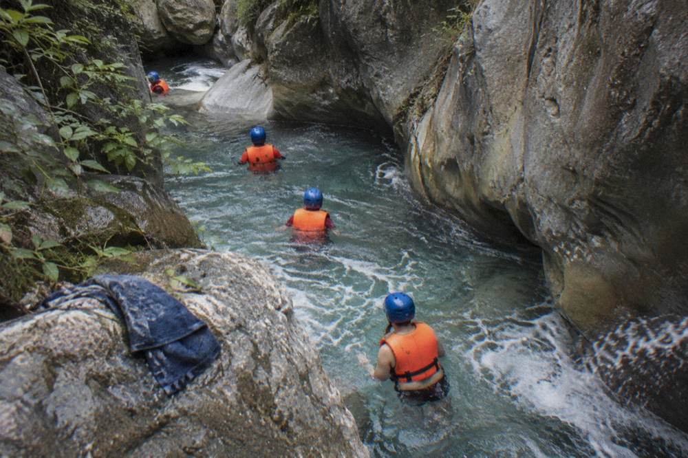 Visitors in helmets and life jackets wading through a clear pool between rock walls
